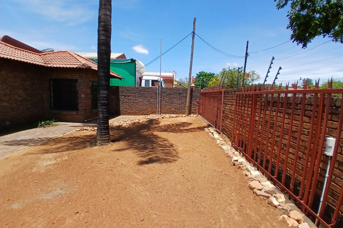 An exterior rear yard area featuring a brick boundary wall, metal security fencing, and an unlandscaped, exposed soil ground surface.