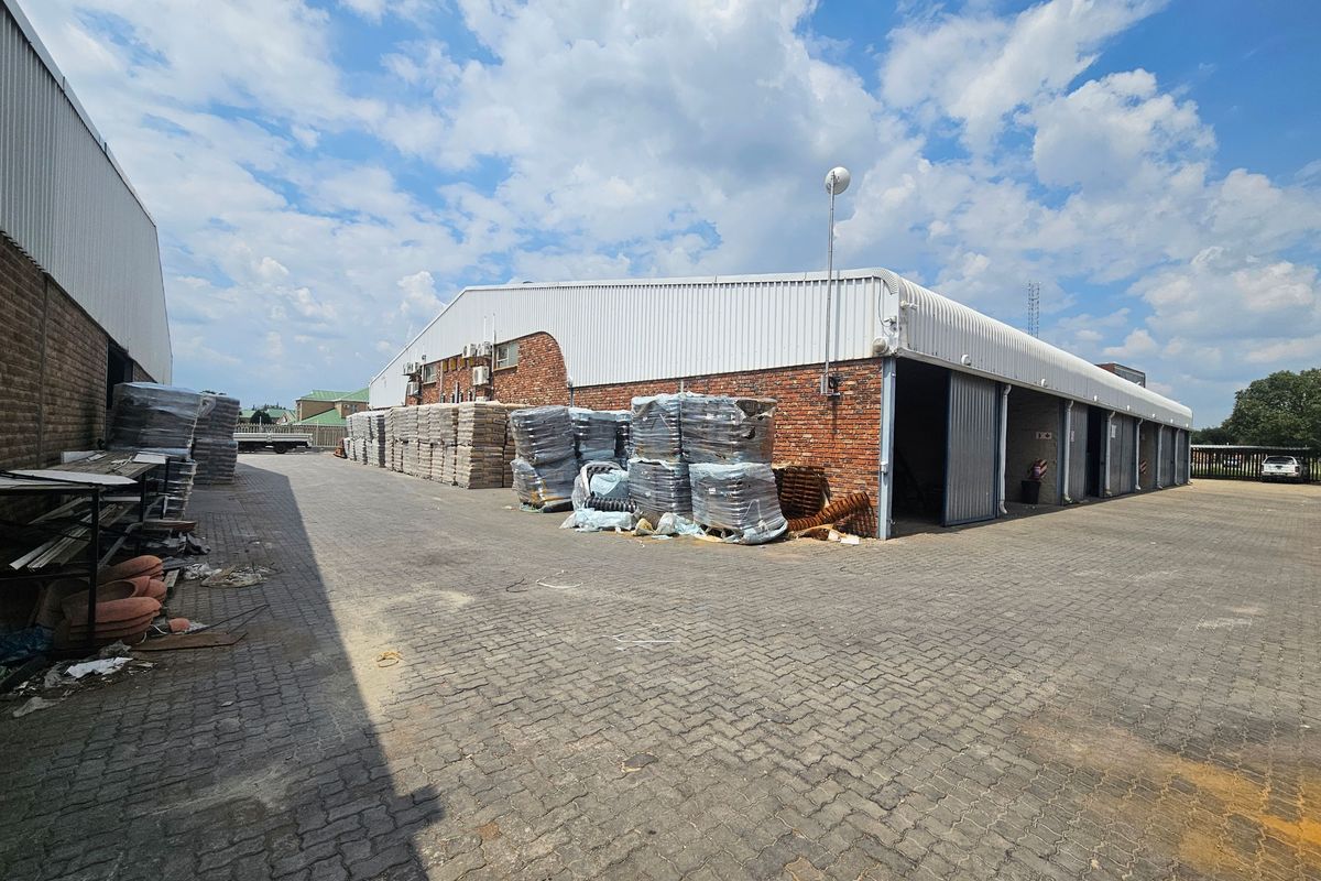Industrial warehouse exterior featuring brick and metal construction, sliding access doors, and a large paved yard area suitable for logistics or storage.