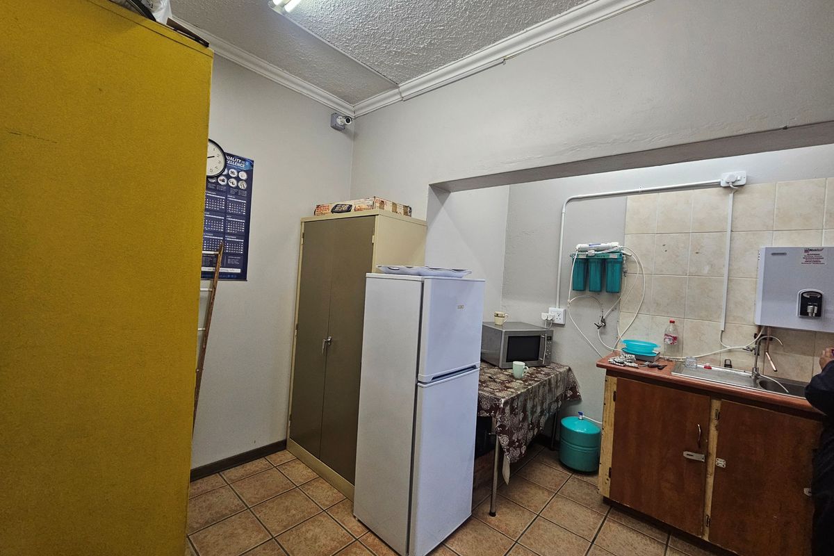 A functional industrial kitchen area featuring tiled flooring, built-in cabinetry with a stainless steel sink, and a wall-mounted water filtration system.