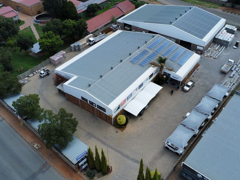 Aerial view of an industrial property featuring a large warehouse with solar panels, paved parking area, and shade cloth carports.