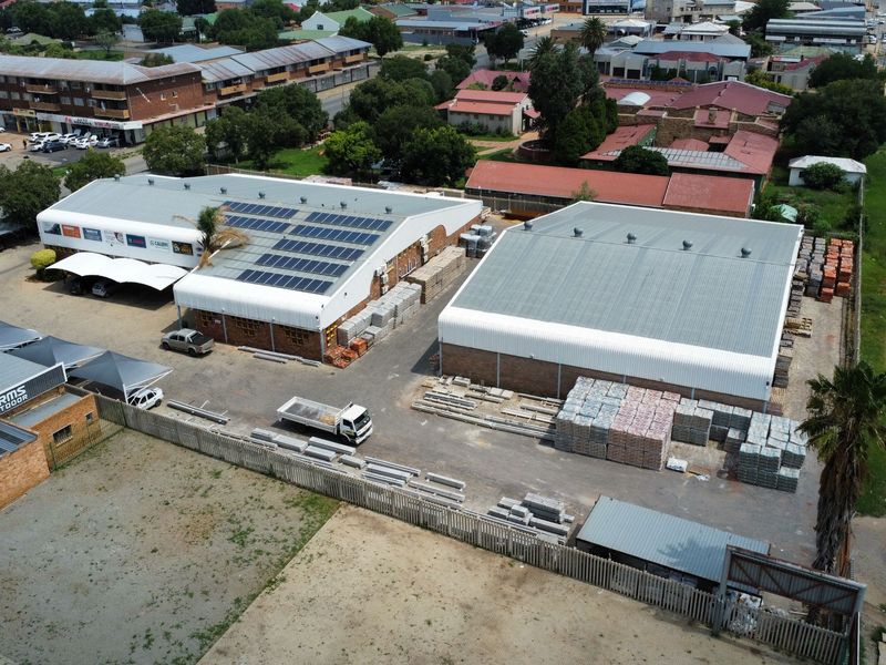 Aerial view of an industrial property featuring two large warehouse buildings with metal roofing, solar panel installations, and a paved yard area.