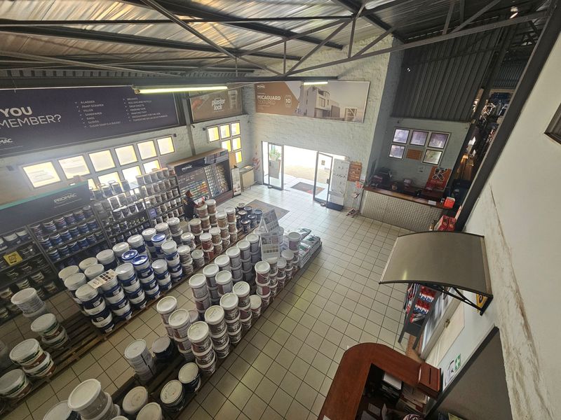 High-ceiling industrial retail space featuring exposed steel trusses, tiled flooring, and a service counter, currently utilized as a paint supply store.