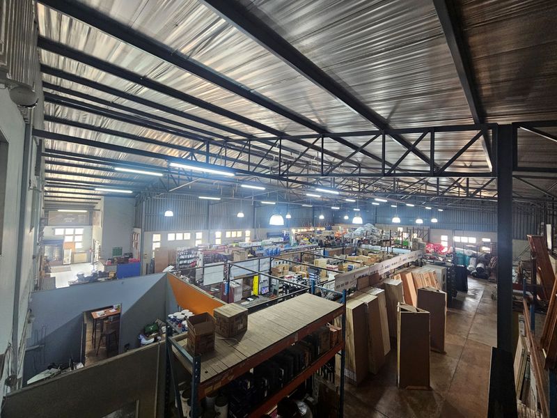 Spacious industrial warehouse featuring high-clearance exposed steel roof trusses, corrugated metal roofing, and extensive fixed industrial shelving units for storage.