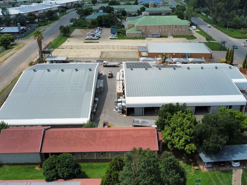 Aerial view of an industrial property featuring multiple warehouse buildings with corrugated metal roofing, solar panel installations, and a paved yard area.