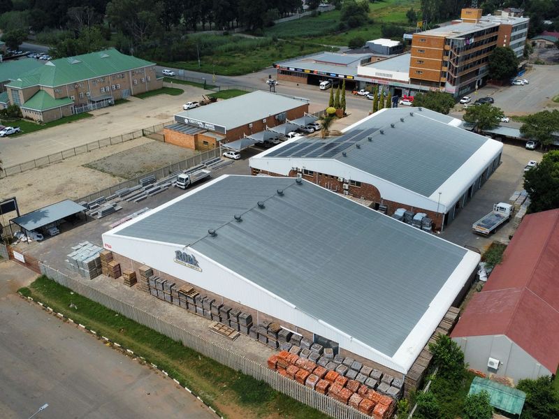 Aerial view of an industrial property complex featuring large warehouse buildings with metal roofing, solar installations, and secure perimeter fencing.