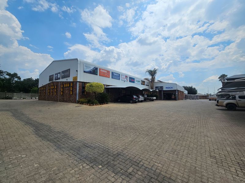 Front exterior view of an industrial warehouse facility featuring a large paved driveway, brick and metal cladding, and covered parking bays.