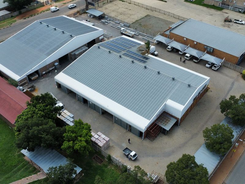 Aerial view of an industrial property featuring multiple warehouse buildings, solar panel installations, paved yard space, and covered parking areas.