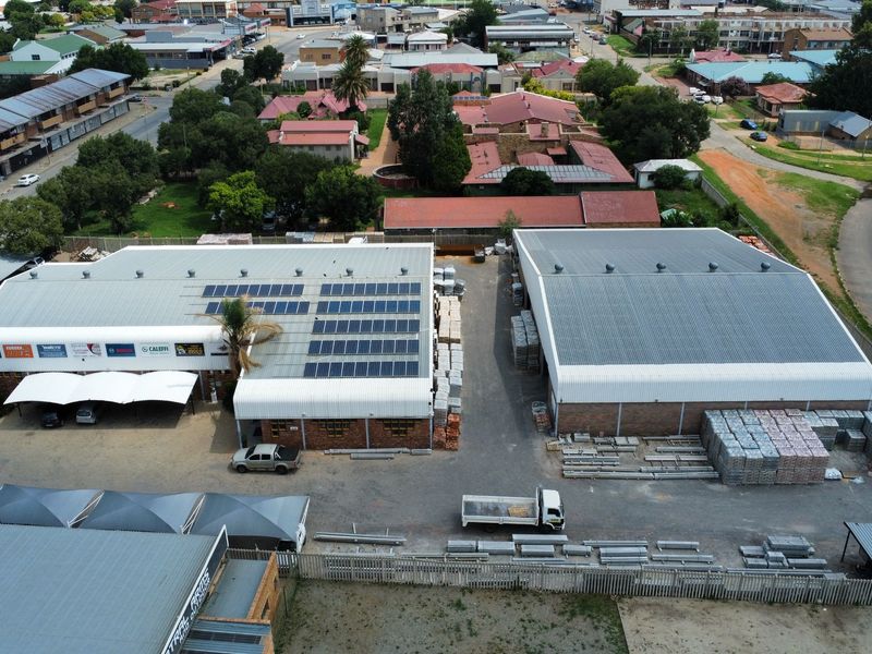 Aerial view of an industrial property featuring two large warehouse buildings with metal roofing, solar panel installations, and a paved yard area.