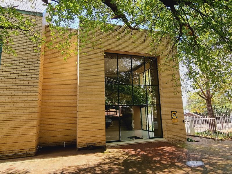 Exterior view of a modern office building featuring a prominent glass facade, brick exterior, and paved driveway entrance.