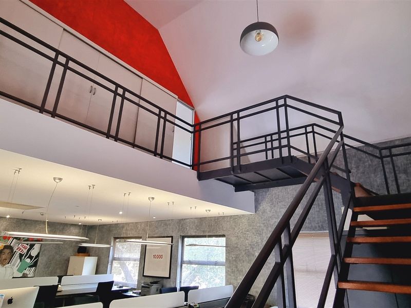 Spacious office interior featuring a mezzanine level, industrial-style metal staircase, vaulted ceilings, and modern recessed lighting.