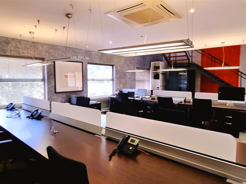 Open-plan office space featuring modern workstations, recessed ceiling lighting, integrated air conditioning, and a staircase leading to an upper level.
