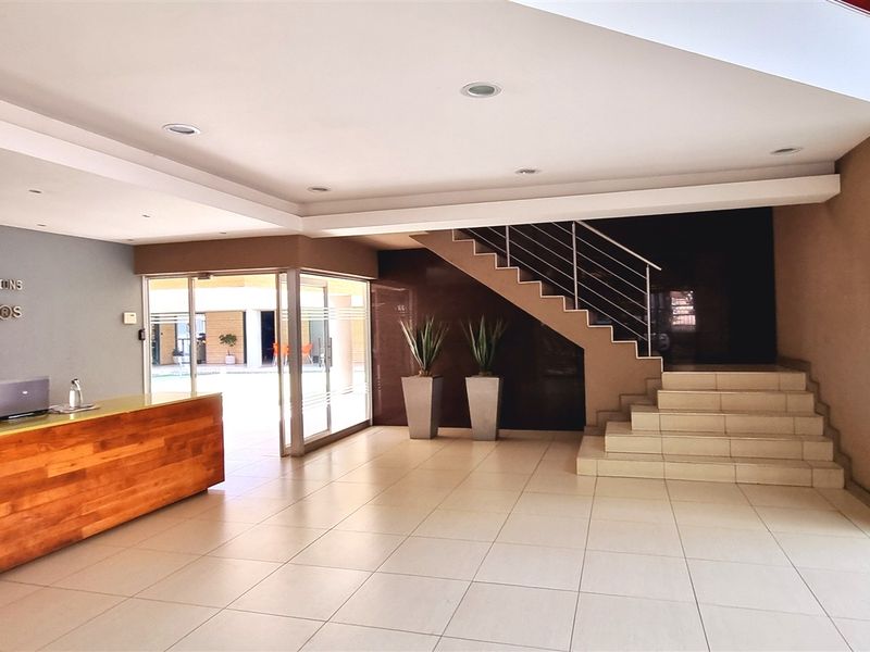 Professional office reception area featuring a built-in wooden reception desk, tiled flooring, and a staircase with a metal railing.