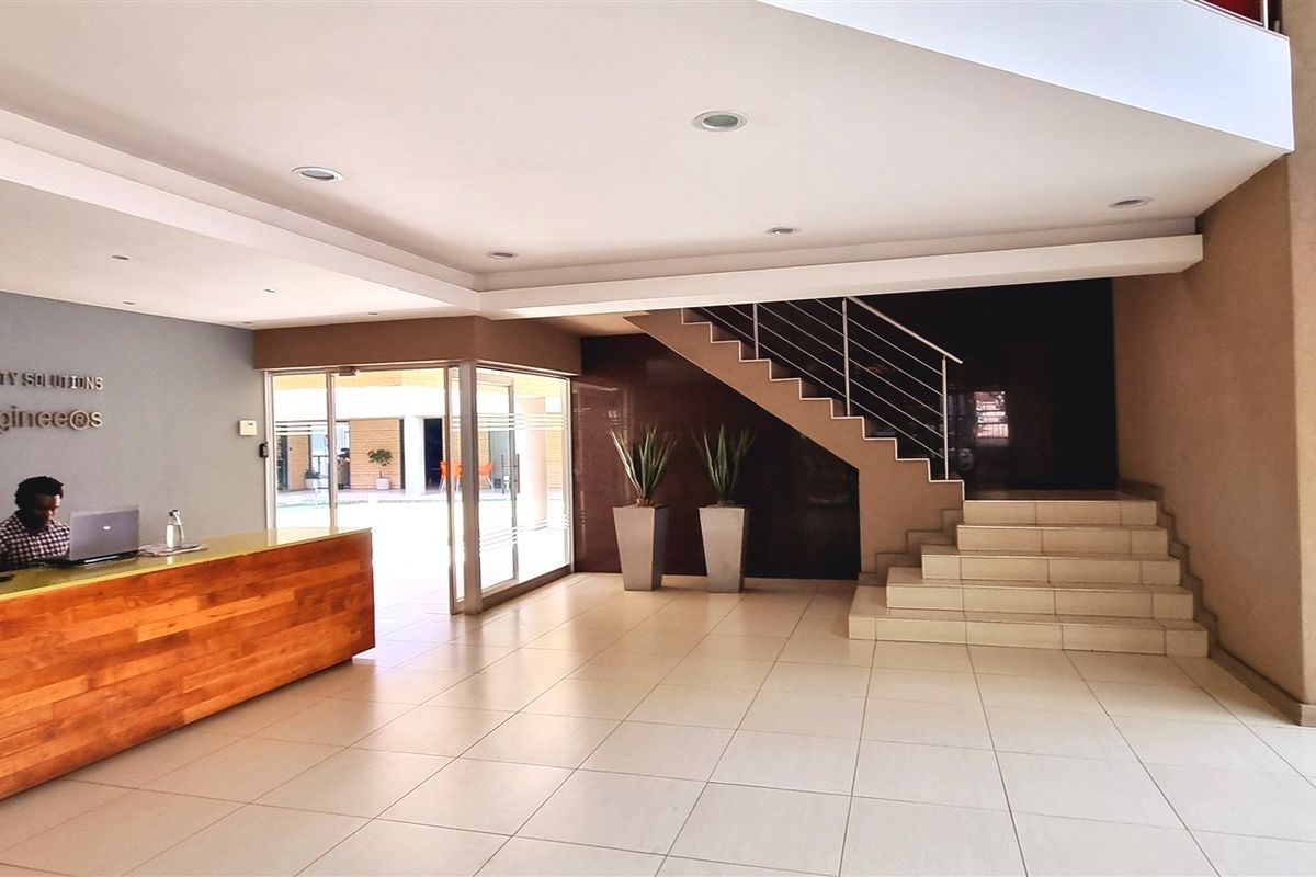 Professional office reception area featuring a built-in wooden reception desk, tiled flooring, and a staircase with a metal railing.