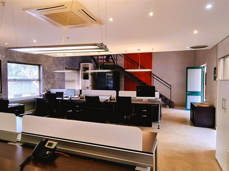 Modern open-plan office space featuring recessed ceiling lighting, integrated air conditioning, and a mezzanine level with a metal staircase.