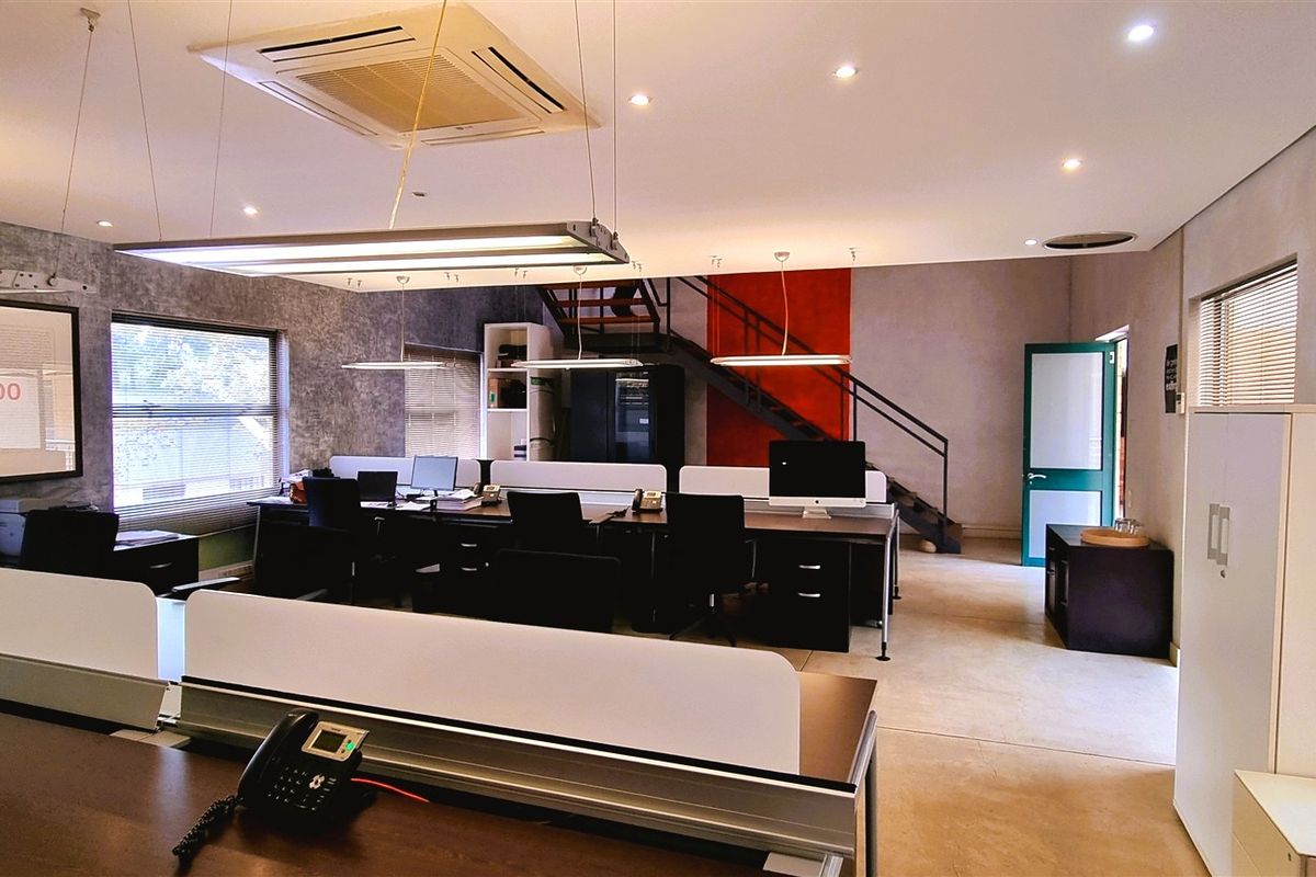 Modern open-plan office space featuring recessed ceiling lighting, integrated air conditioning, and a mezzanine level with a metal staircase.