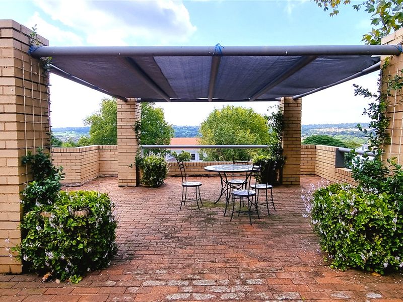 An elevated outdoor patio area featuring brick paving, brick pillars, and a shade sail structure, offering expansive views.