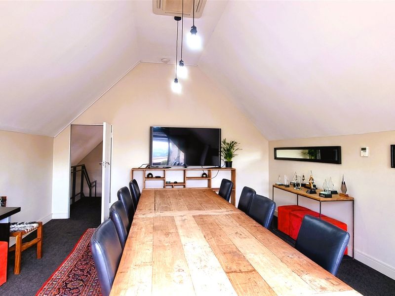 A spacious attic-style office featuring vaulted ceilings, recessed lighting, and dark carpeting, providing a functional and professional workspace environment.