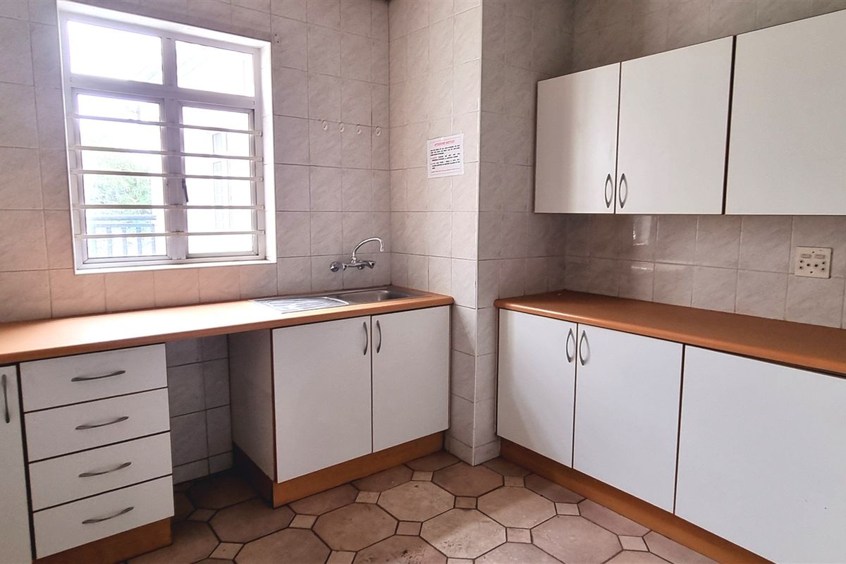 A functional office kitchenette featuring built-in cabinetry, laminate countertops, a stainless steel sink, and tiled wall finishes.