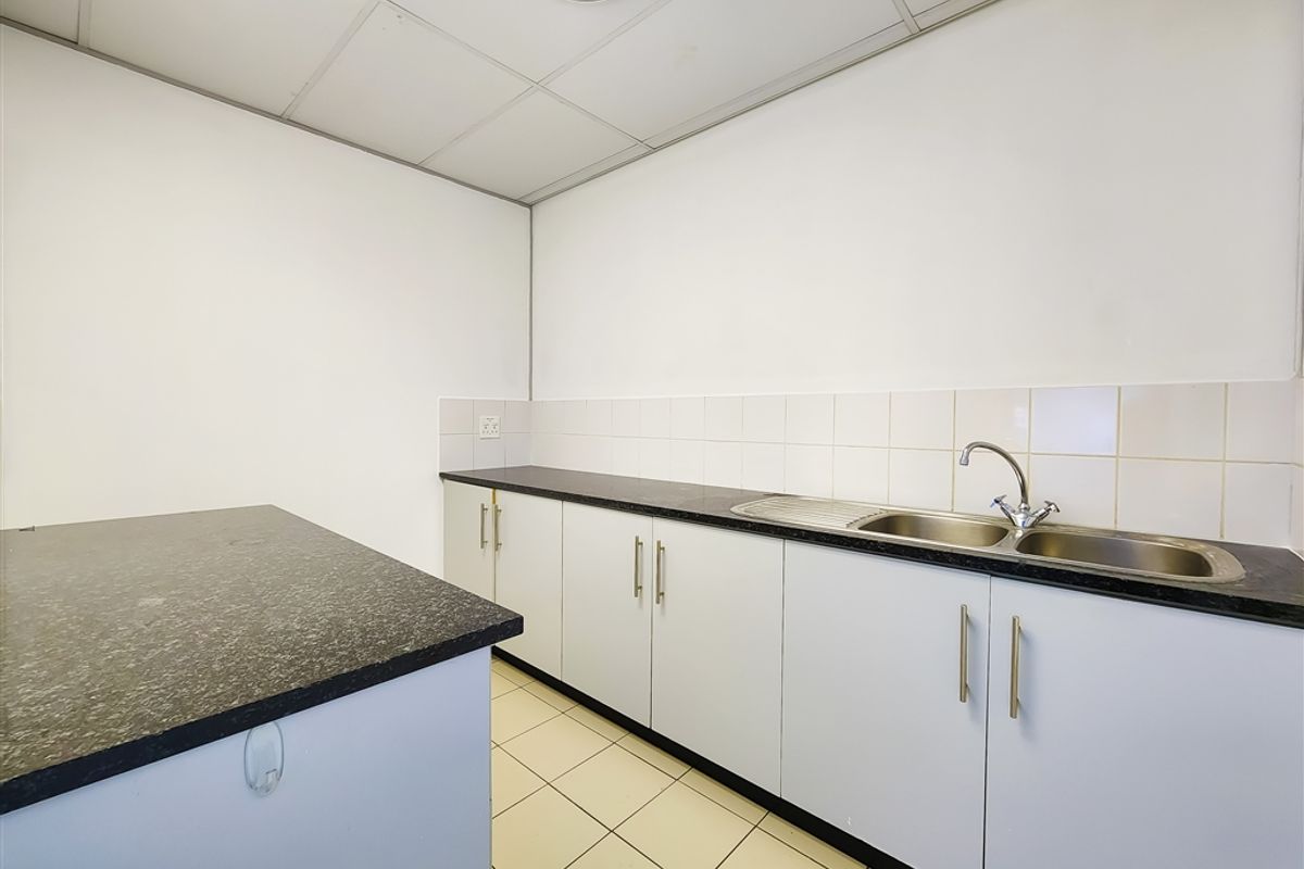 A functional office kitchenette featuring white cabinetry, dark granite-style countertops, a stainless steel double sink, and tiled flooring.