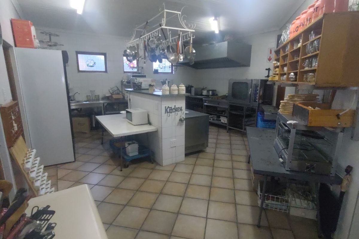 A functional commercial kitchen featuring stainless steel prep surfaces, a commercial oven, extractor fan, and tiled flooring, suitable for high-volume food preparation.