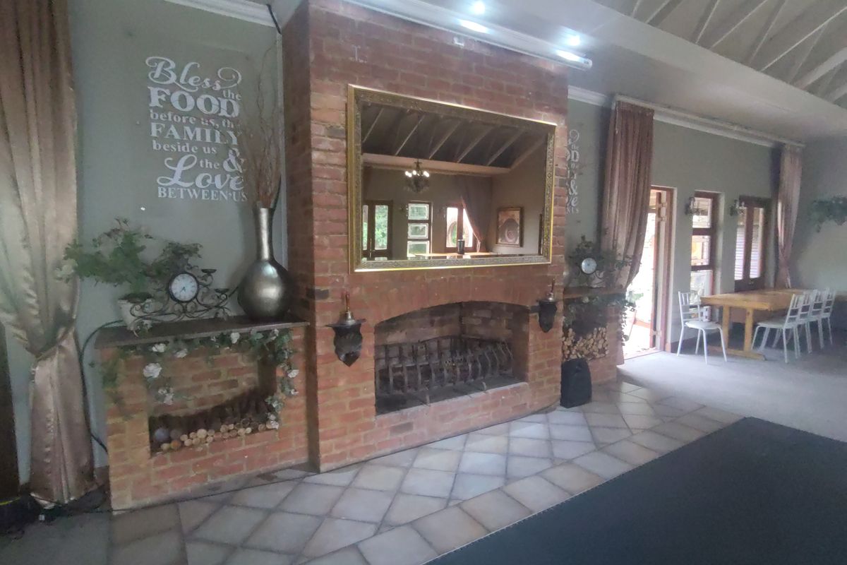 Spacious living area featuring a prominent brick fireplace, tiled flooring, and exposed beam ceilings, offering a warm and inviting atmosphere.