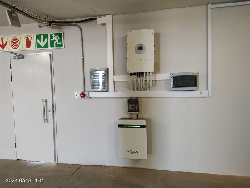Utility area featuring a wall-mounted solar inverter, lithium battery storage system, and electrical distribution board with clear fire safety signage.