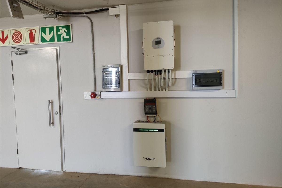 Utility area featuring a wall-mounted solar inverter, lithium battery storage system, and electrical distribution board with clear fire safety signage.