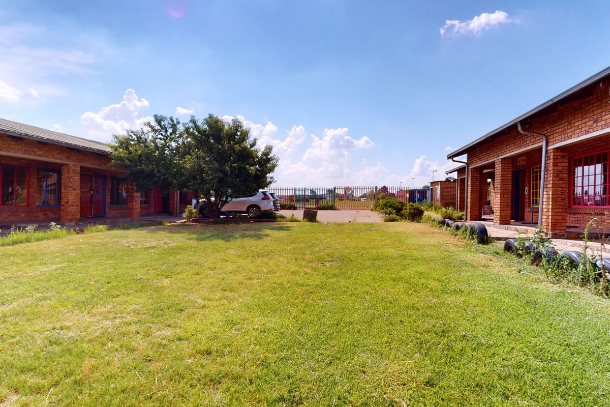 Exterior view of a commercial property complex featuring face brick buildings, metal security fixtures, and a central courtyard area with lawn and paved access.