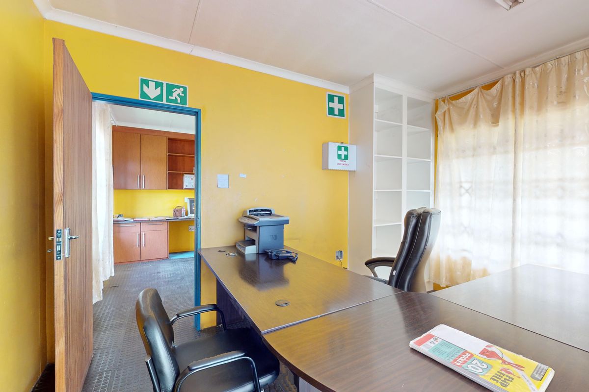 A functional office space featuring built-in shelving, emergency signage, and direct access to an adjacent kitchenette area.