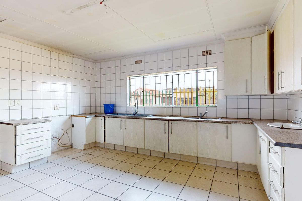 A spacious, empty kitchen featuring tiled surfaces, built-in cabinetry, and a double sink, requiring cosmetic updates and minor repairs to reach its full potential.