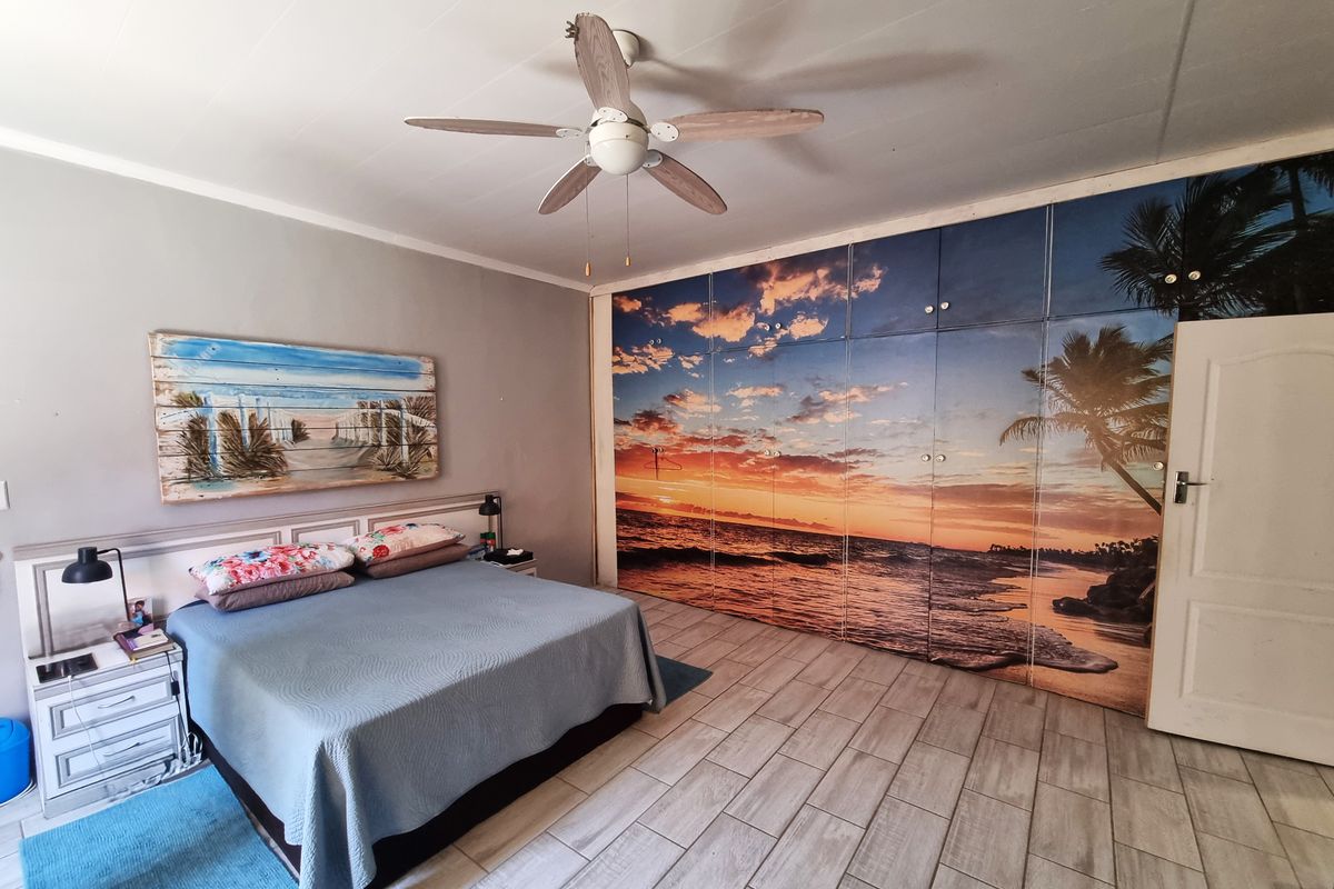 Spacious bedroom featuring large built-in cupboards with a decorative sunset mural, tiled flooring, and a ceiling fan.