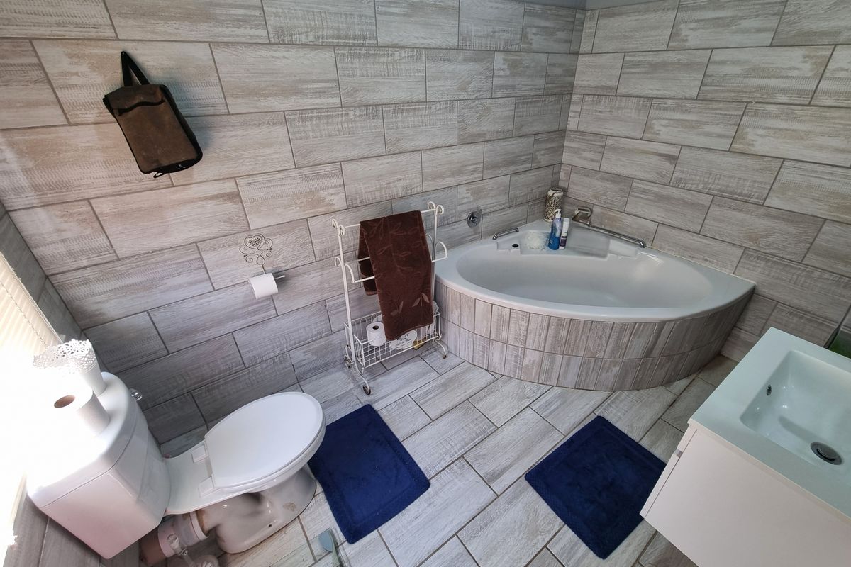 A modern bathroom featuring wood-look wall and floor tiling, a corner bathtub, a white vanity basin, and a standard toilet.