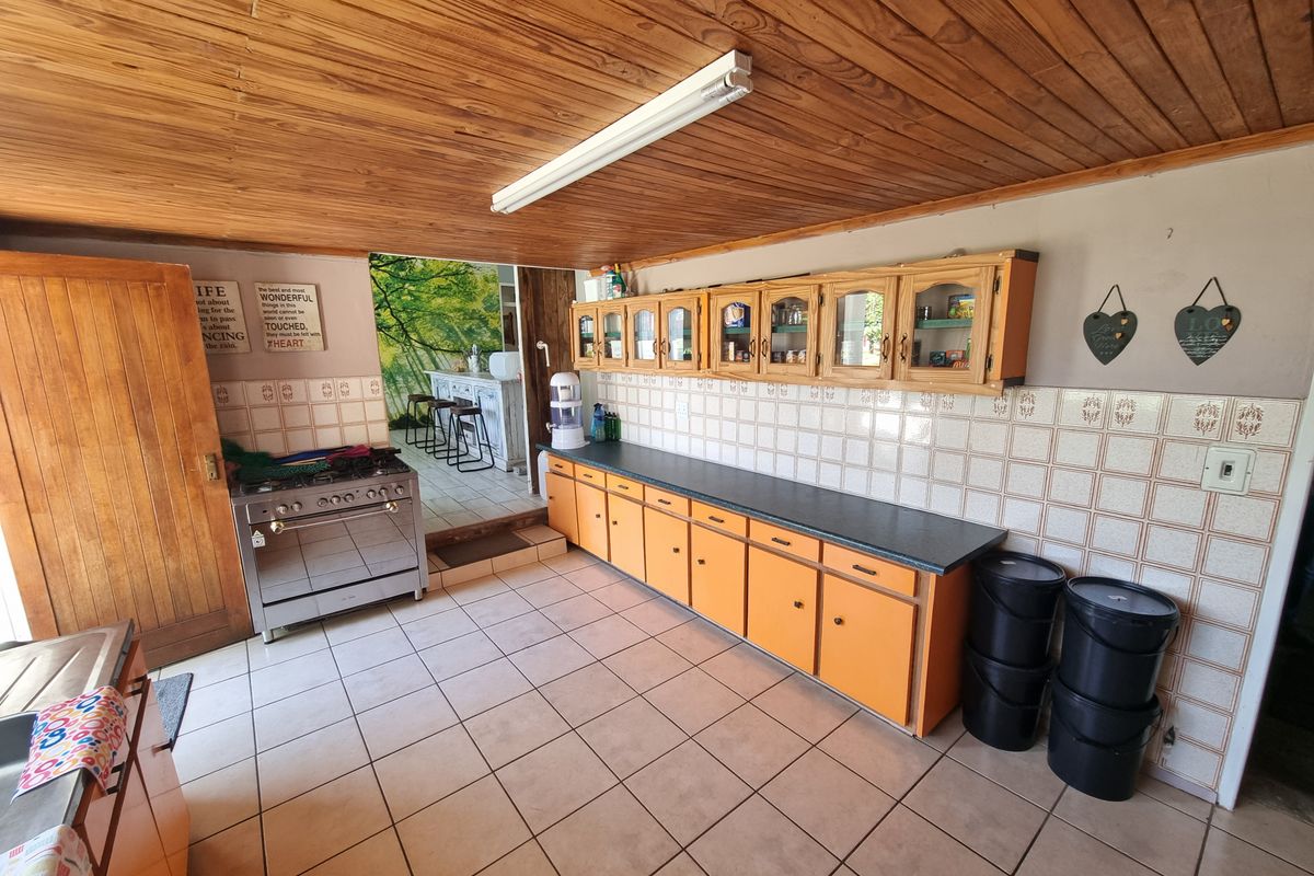 A functional kitchen featuring wooden cabinetry, tiled flooring, a tiled backsplash, and a freestanding gas stove, with an adjacent open-plan area.