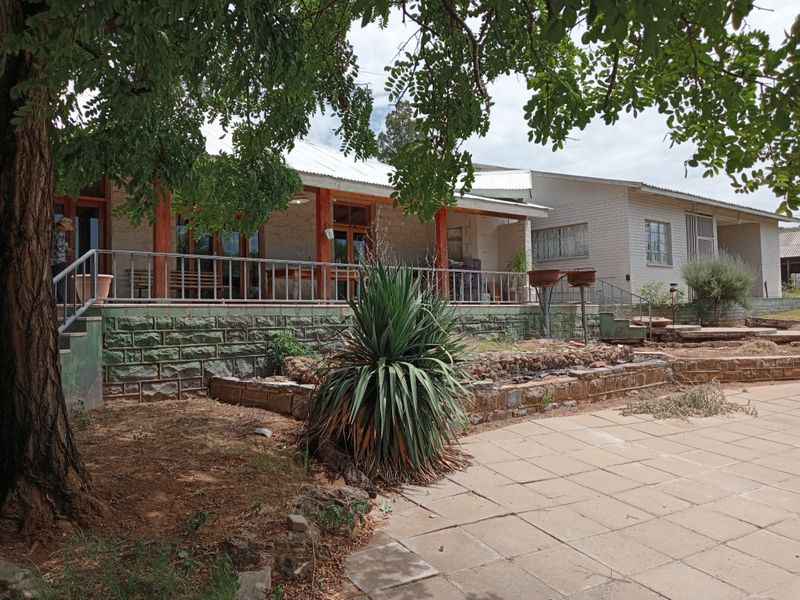Rear view of the farmhouse featuring a covered patio with timber posts, stone masonry base, and a paved outdoor terrace area.