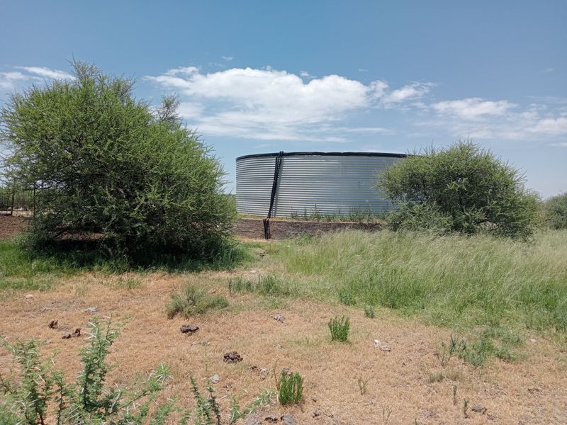 A large corrugated steel water storage tank situated on a brick base within a rural farm landscape.