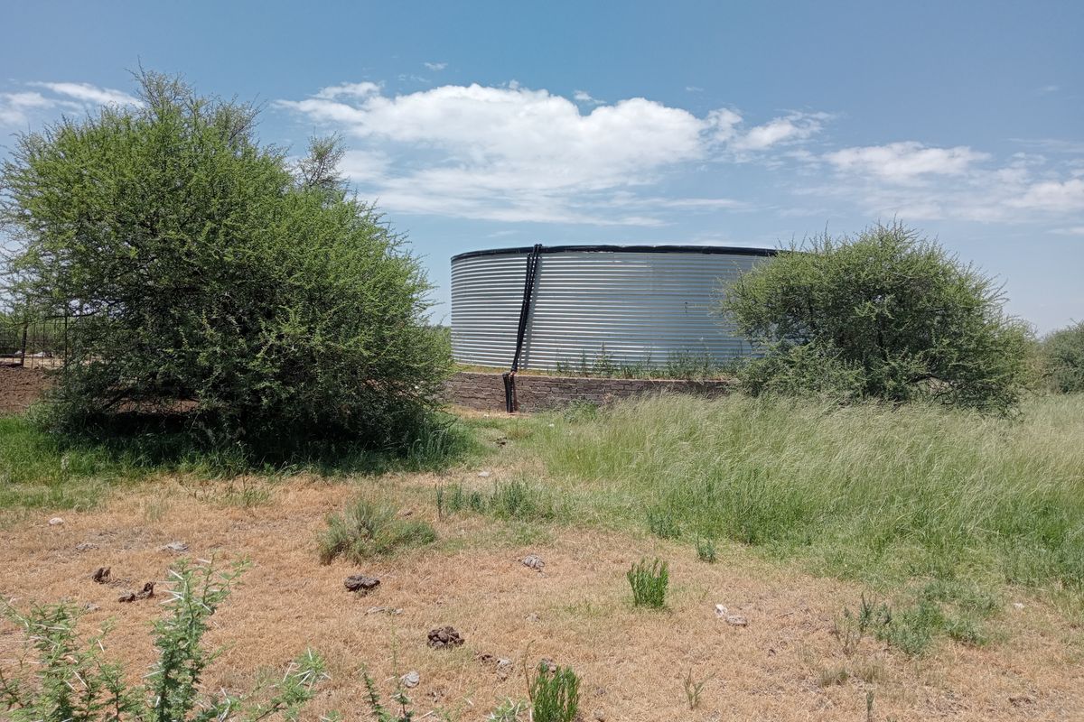 A large corrugated steel water storage tank situated on a brick base within a rural farm landscape.