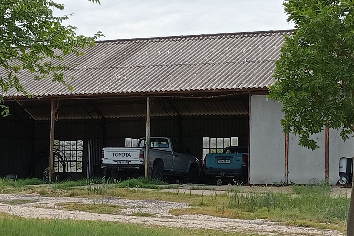 An open-sided farm shed or garage structure featuring a corrugated metal roof and steel support columns, suitable for vehicle storage.