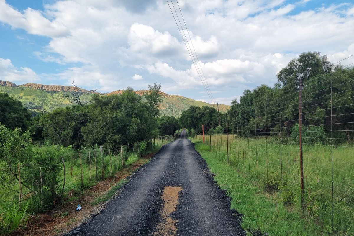 A gravel access road leading through the property, bordered by wire fencing and natural vegetation with mountain views in the background.