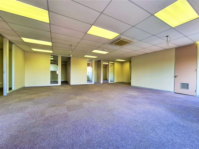 A spacious, empty open-plan office area featuring suspended ceilings, recessed lighting, integrated air conditioning, and glass partition walls.