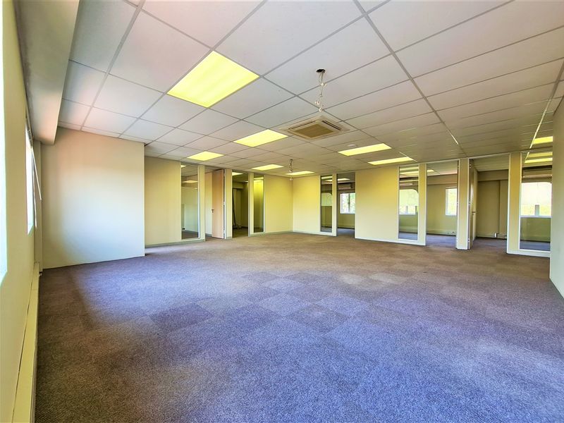 Spacious open-plan office area featuring suspended ceilings, recessed lighting, carpeted flooring, and glass partition walls, providing a versatile and professional workspace.