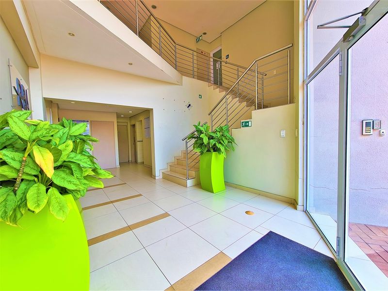 Bright and spacious office building entrance foyer featuring tiled flooring, a modern staircase with stainless steel balustrades, and large glass entrance doors.