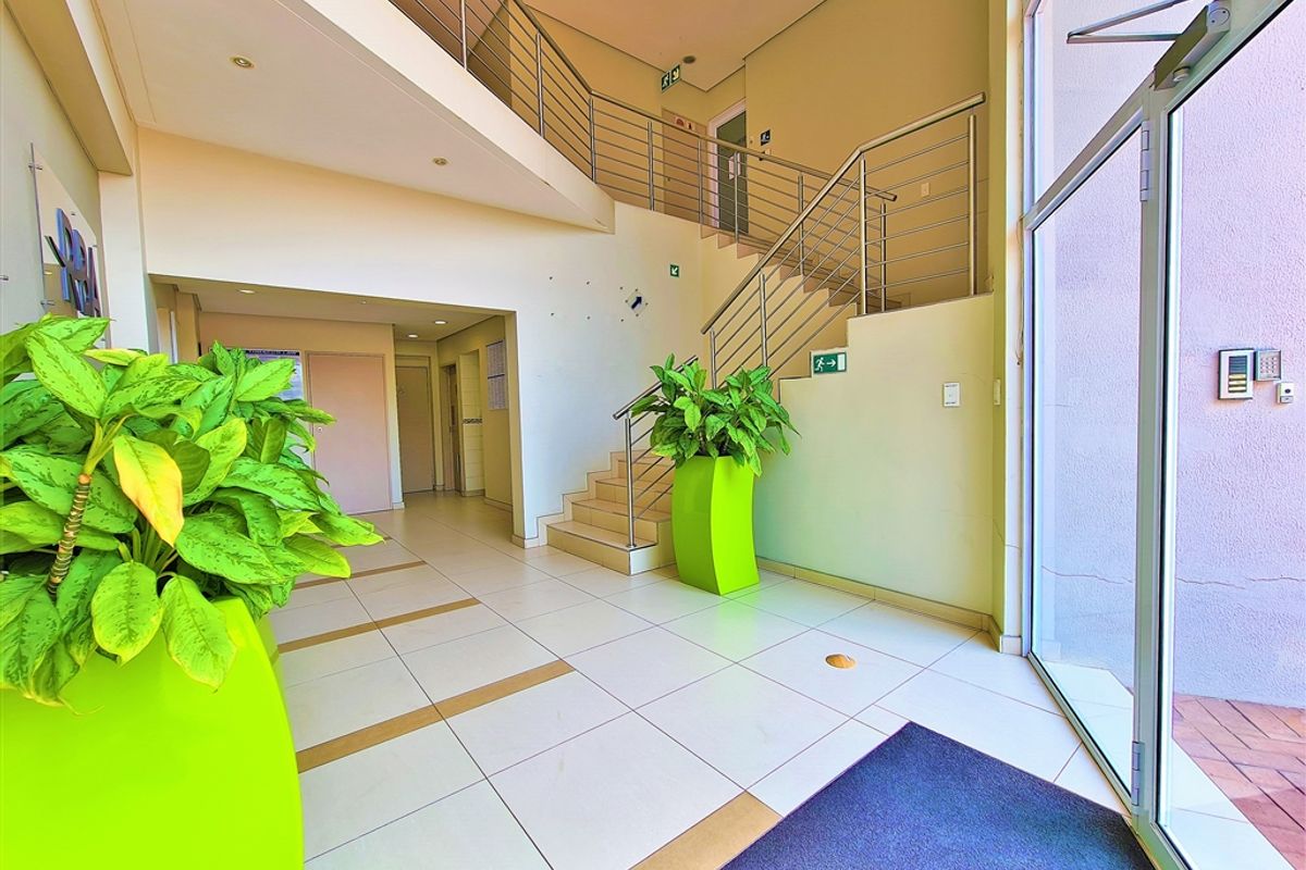 Bright and spacious office building entrance foyer featuring tiled flooring, a modern staircase with stainless steel balustrades, and large glass entrance doors.