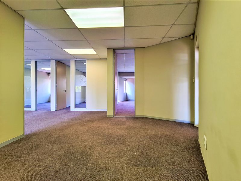 An empty office space featuring carpeted flooring, suspended ceilings with recessed lighting, and internal partitions creating multiple work areas.