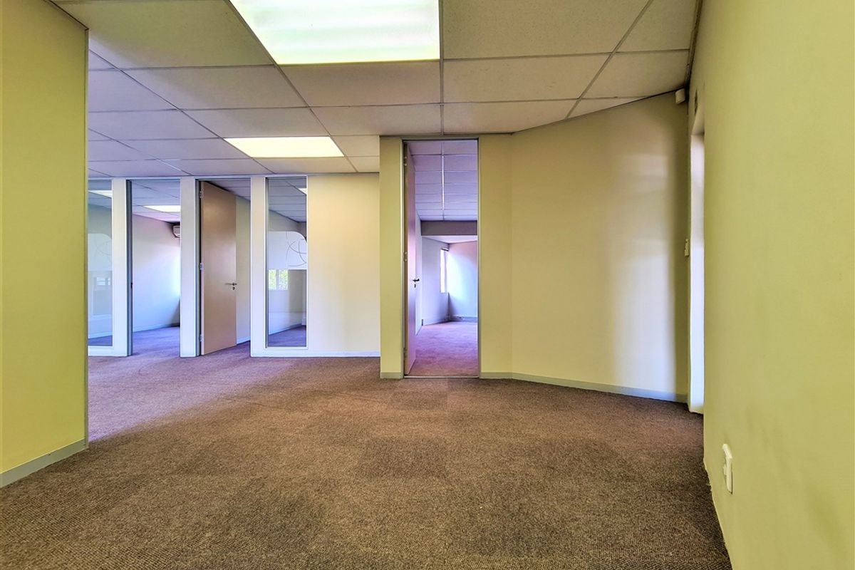An empty office space featuring carpeted flooring, suspended ceilings with recessed lighting, and internal partitions creating multiple work areas.