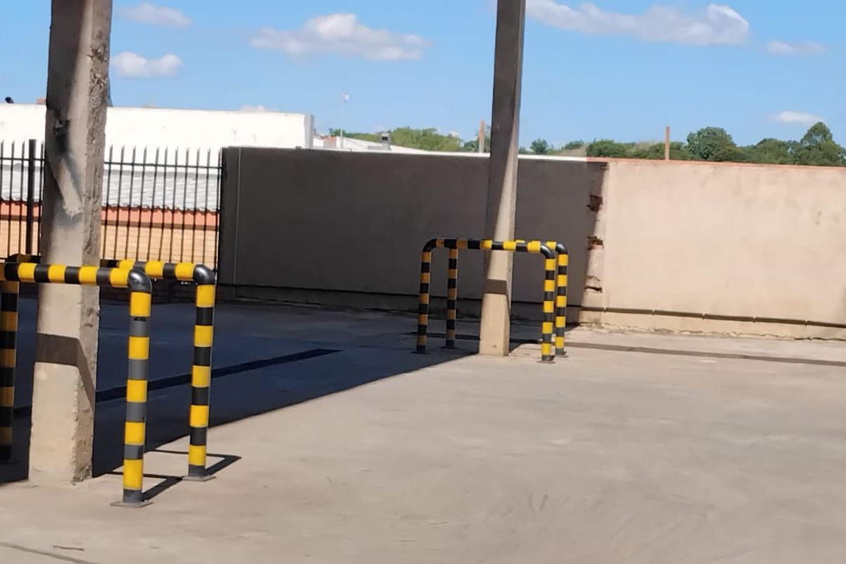 Industrial exterior yard area featuring concrete hardstand, protective steel bollards, and a perimeter wall with access to a roller shutter door.