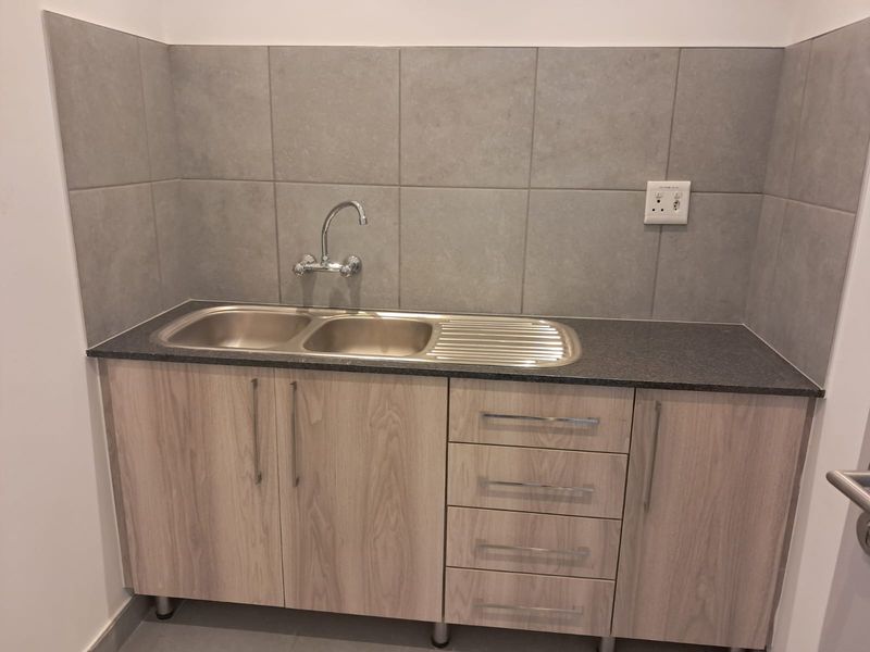 A clean and modern scullery area featuring a stainless steel double sink, laminate cabinetry, and neutral tiled splashback.