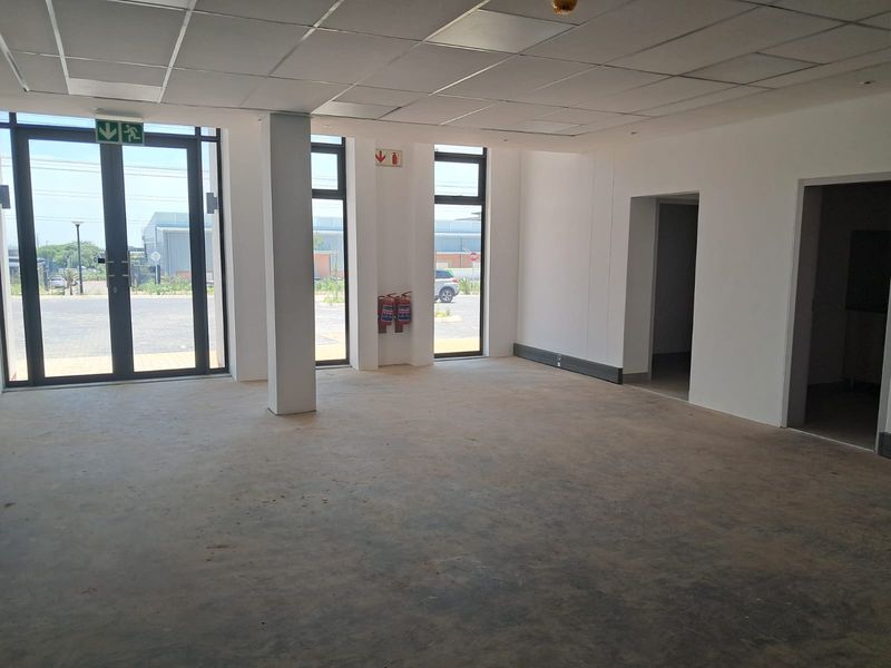 An open-plan industrial office space featuring a suspended ceiling, large aluminium-framed glass doors, and concrete flooring, ready for custom fit-out.