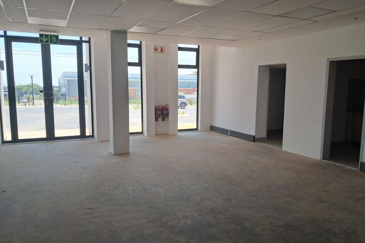 An open-plan industrial office space featuring a suspended ceiling, large aluminium-framed glass doors, and concrete flooring, ready for custom fit-out.