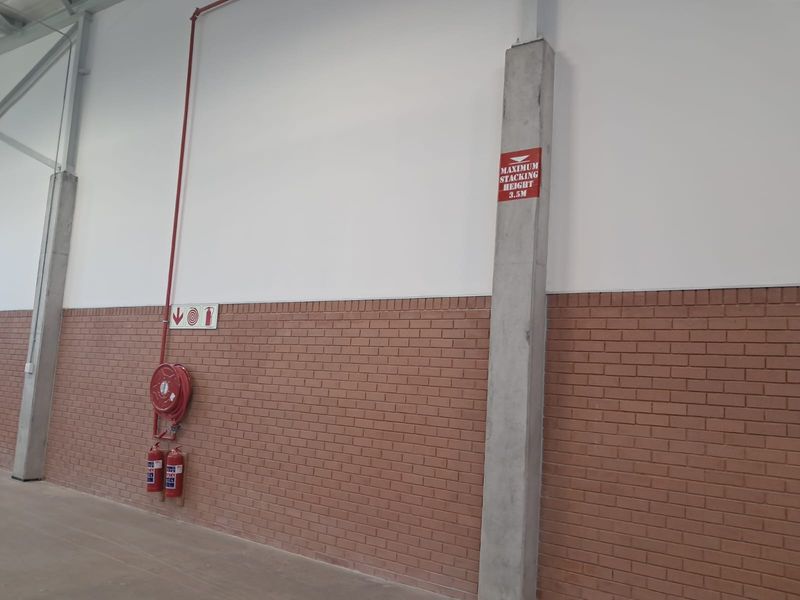 Industrial warehouse interior featuring concrete support columns, brick wall finish, and integrated fire safety equipment including a hose reel and extinguishers.