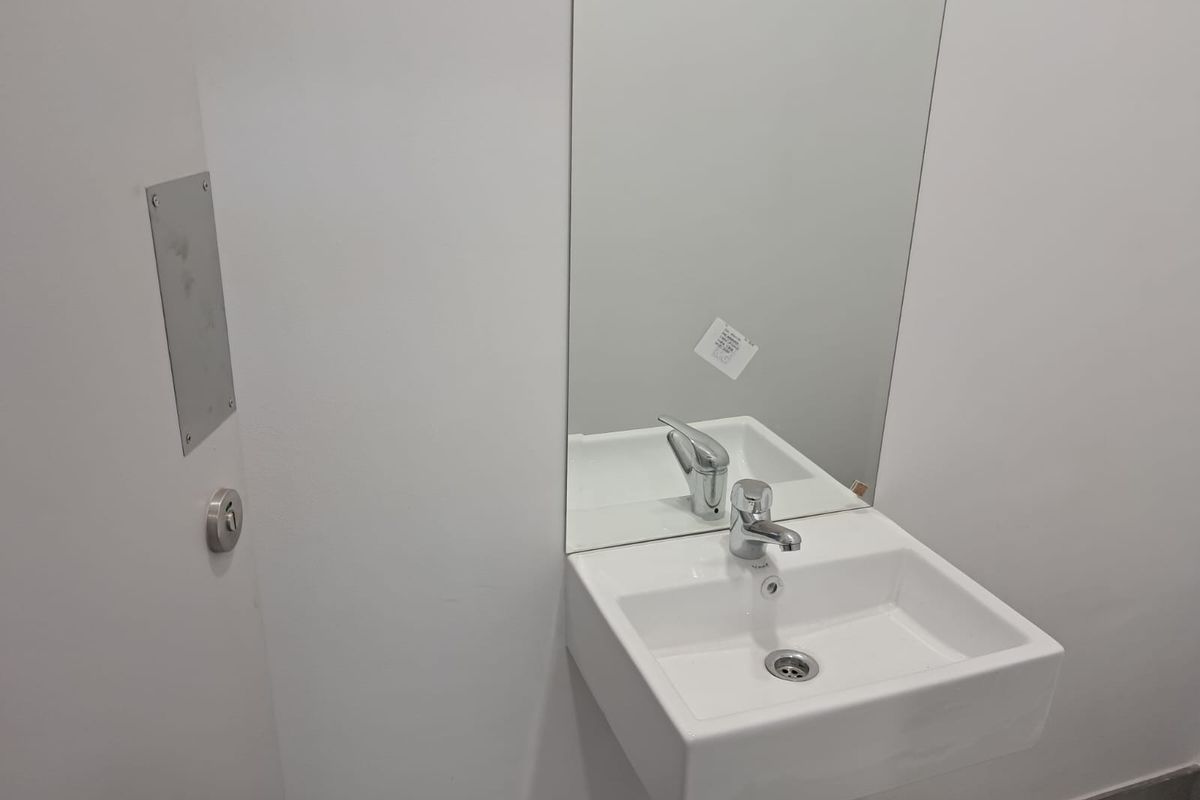 A clean, minimalist bathroom featuring a wall-mounted white basin with a chrome mixer tap and a large wall mirror.